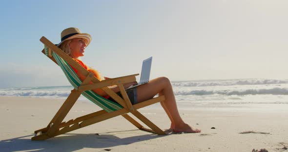 Woman with hat using laptop at beach in the sunshine 4k