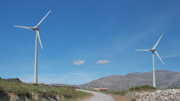 Two Wind Turbines and Road In-between in Hill Landscape on Sunny Day