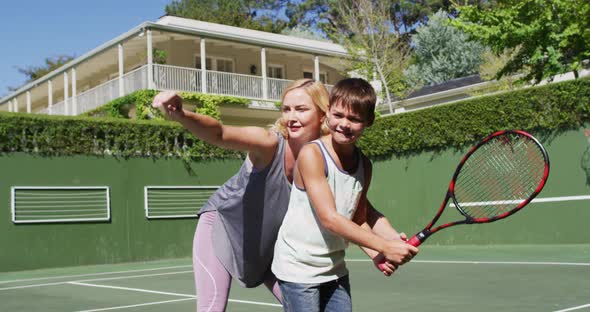 Caucasian mother teaching her son to play tennis at tennis court on a bright sunny day alt