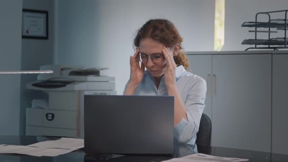 Portrait of Tired Young Businesswoman Using Laptop Computer at Office Desk alt