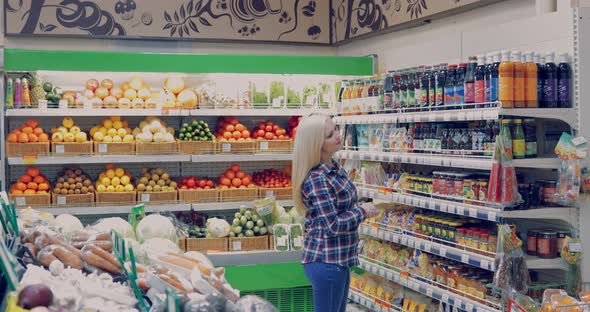 Attractive Woman is Walking Near the Supermarket Shelf and Selects the Products alt