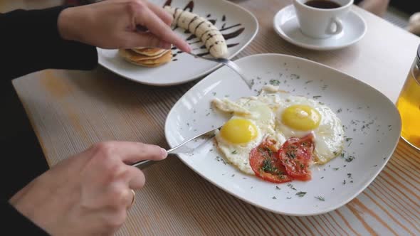 Female Hands Close-up with Fork and Knife Over Scrambled Eggs. Woman Having Breakfast, Close Up alt