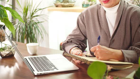 Modern Senior Business Lady Writing Company Profit in Her Notebook. alt