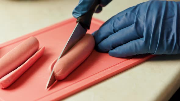 Hands in Blue Gloves Cut Raw Sausages in Half Lengthwise alt