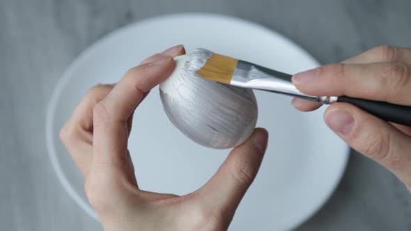 Close-up. Female hands paint Easter egg in a modern minimalist style with colorful paint.