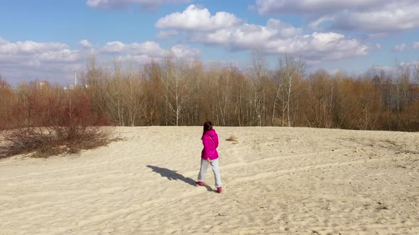 A Girl In a Bright Winter Jacket Walks On the Sand