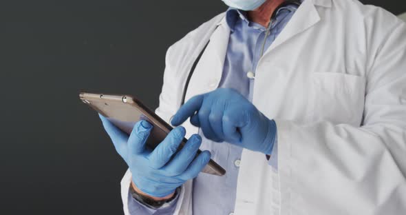 Mid section of caucasian male doctor wearing surgical gloves using digital tablet alt
