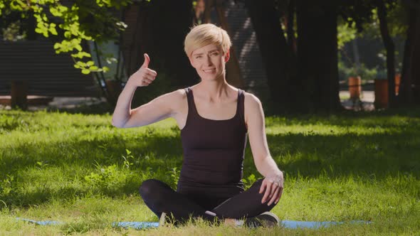 Middleaged Caucasian Woman Mindfulness Slender Lady Trainer Sits on Mat on Grass Lawn in Lotus alt