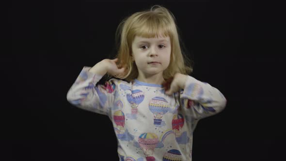 Little Baby Girl in Pajama Is Fooling Around and Make Faces. Black Background alt