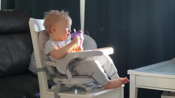 Cute Kid with Baby Straw Feeding Cup Sitting in Booster Seat One Year Old Toddler Watching Tv alt