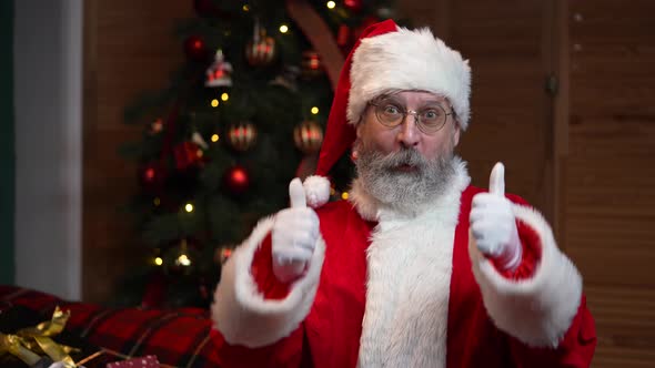 Portrait of Santa Claus Looking at Camera Listens Attentively and Makes a Thumbs Up Gesture alt