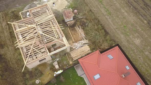 Top down aerial view of two private houses, one under construction with wooden roofing frame  alt