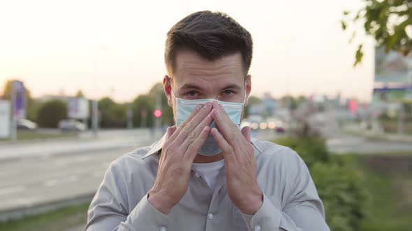 A Young Caucasian Man Puts on a Face Mask Looks at the Camera Then Takes It Off in an Urban Area alt