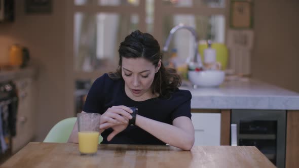 Young adult woman using smart watch at home on kitchen table