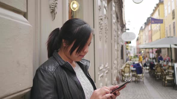 Asian woman standing and using smartphone in town alt