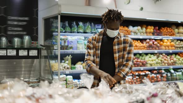 Man in Mask Push Cart Choosing Fruits and Vegetables in the Fresh Produce Section alt
