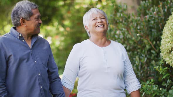 Video of happy biracial senior couple holding hands and walking in garden alt