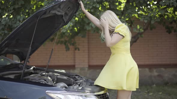 Side View Portrait of Gorgeous Slim Blond Woman Opening Car Hood and Holding Head with Hands alt