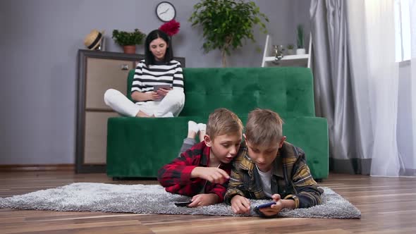 Mother and Her Two Sons which Spending Their Leisure at Watching Interesting Apps on Phones alt