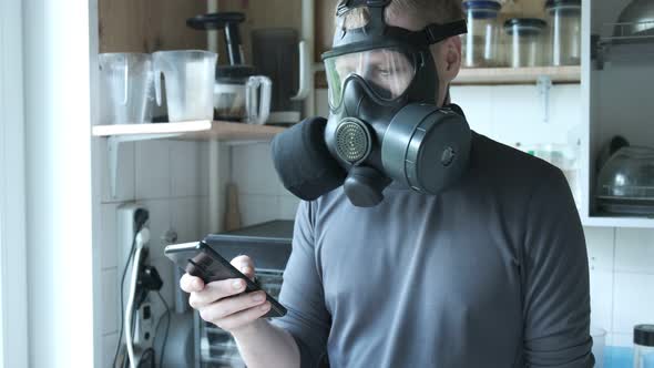 Young Man in Gas Mask Speaking Smartphone at Kitchen at Home