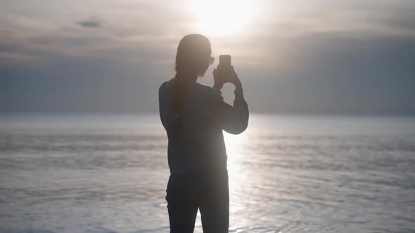 Silhouette of Young Woman Shooting Sea and Amaizing Sunset View on Smartphone