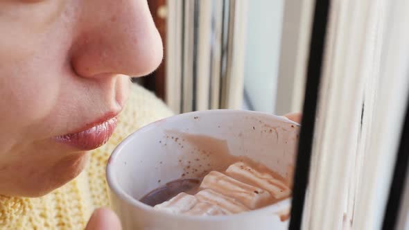 Extreme Closeup of a Woman's Face Drinking Cocoa with Marshmallows From a Mug