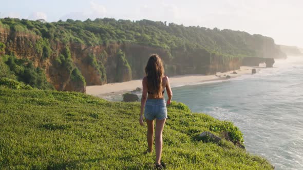 ASia Woman Hiking Cliff Ocean Beach with High Green Grass at Shore of Wild Sumba Island Indonesia