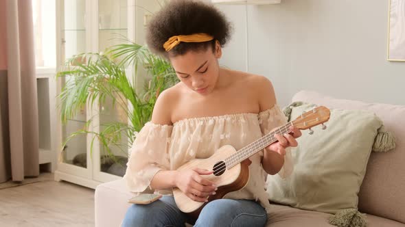 African american woman taking online ukulele music guitar lessons tutorial with phone app alt