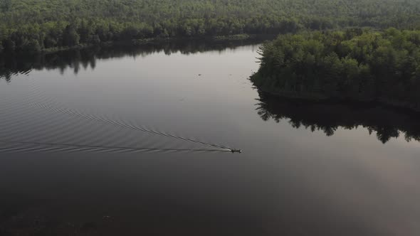 Static aerial shot over flat calm lake lake boat travels across surface surrounded by wilderness alt