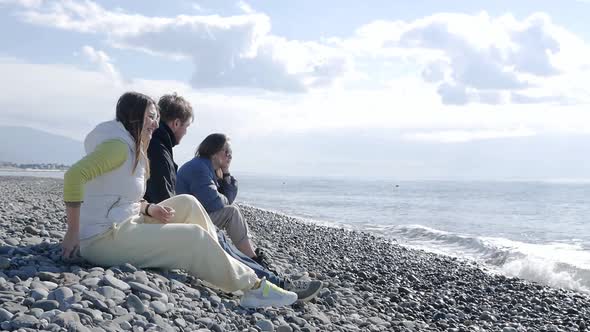 Friends are Sitting on the Shore of a Stone Beach By the Sea