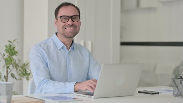 Middle Aged Man with Laptop Smiling at the Camera alt