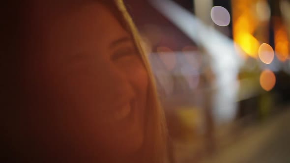 Teenage girl making faces and covering camera lens with hand outdoors at night