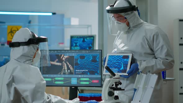 Doctors in Coveall Discussing About Virus Development in Front of Pc and Tablet alt