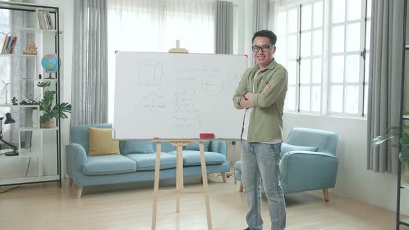 Asian Male Teacher With Glasses Crossing Arms And Smiling To Camera While Teaching Math At Home alt