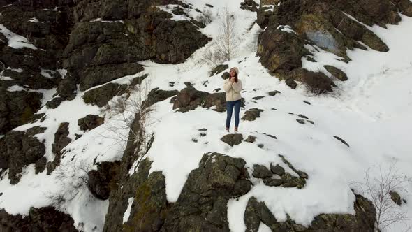 A Girl in a Beige Jacket Stands on Top of a Snowy Mountain and Warms Her Hands