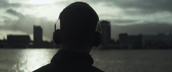 Back view of a man listening music in front of the river and slowly dancing alt