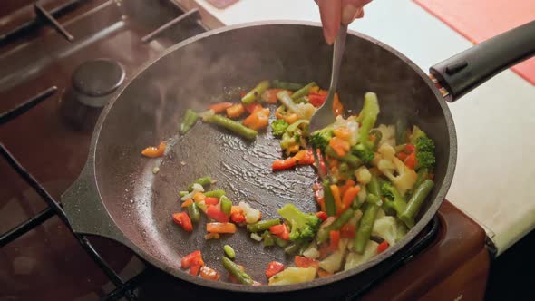 Caucasian Hand Stirring Vegetables in a Frying Pan with Stainless Steel Fork While Frying Closeup