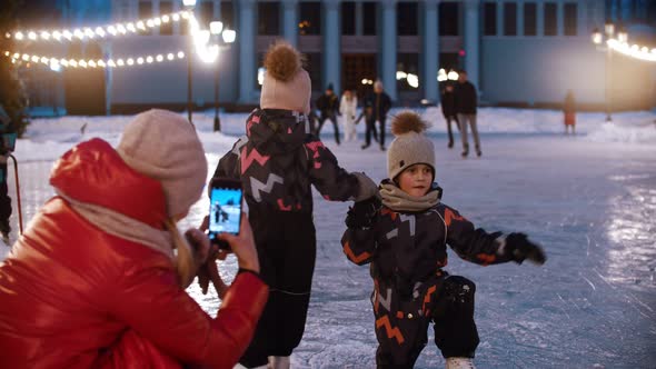 Two Little Kids Dancing on the Ice Rink - Their Mother Shooting Them on the Phone Camera alt