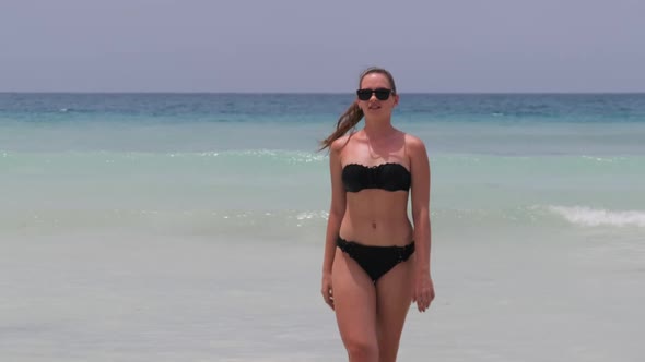 Young Woman in a Black Swimsuit Walks From the Turquoise Ocean on Paradise Beach alt