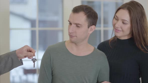 Portrait of a Happy Couple Receiving the Keys From an Unrecognized Real Estate Agent and Joyfully alt