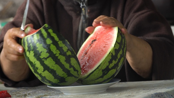 An adult woman's hands with a knife are cutting a ripe watermelon closeup alt
