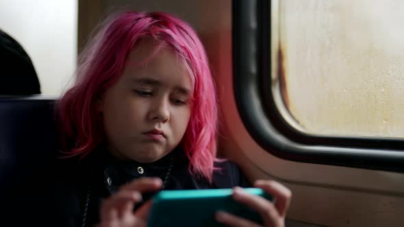 Pretty Modern Little Girl with Pink Hair is Riding Train and Watching Cartoons By Smartphone alt