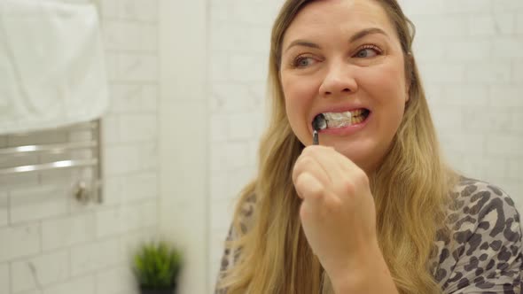 Woman with Long Blond Hair Brushing Her Teeth with Toothpaste in Front of a Mirror alt