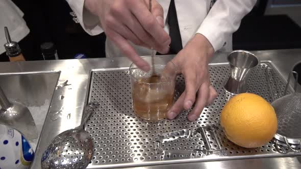 Speakeasy bartender making cocktail, stirring liquor with bar spoon.
