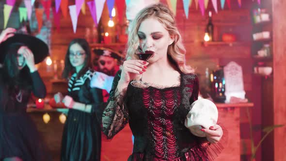 Vampiress Fulfills Her Taste of Blood at a Halloween Party with a Skull in Her Hands alt