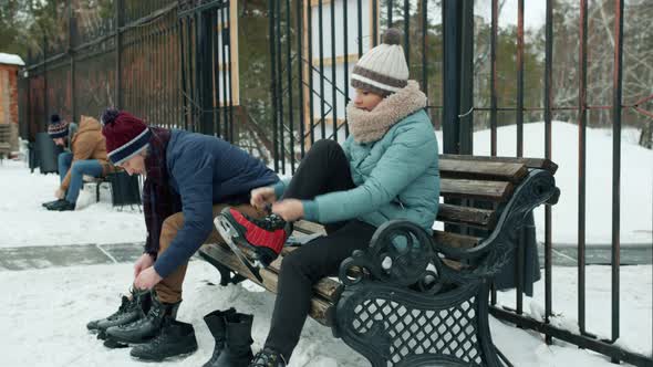 People Putting on Ice Skates Sitting on Bench at Skating Rink in Winter Park alt