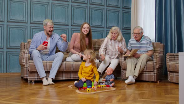 Multigenerational Family Leisure at Home Motivating Shouting to Child Kid Girl Playing Railway Toy alt