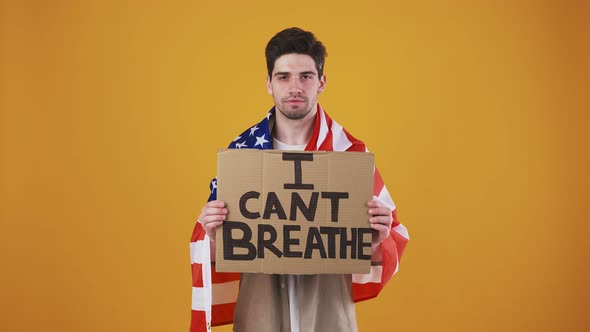 Young Guy Wrapped in Flag of USA is Raising Up Cardboard Tablet with Inscription I Cant Breathe alt