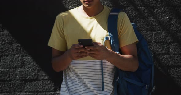 Mid section of mixed race man wearing headphones and using smartphone in the street alt