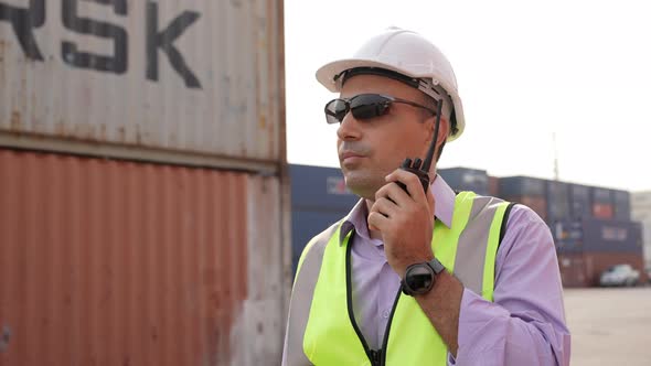 Engineer foreman talking on walkie-talkie with colleague in container warehouse